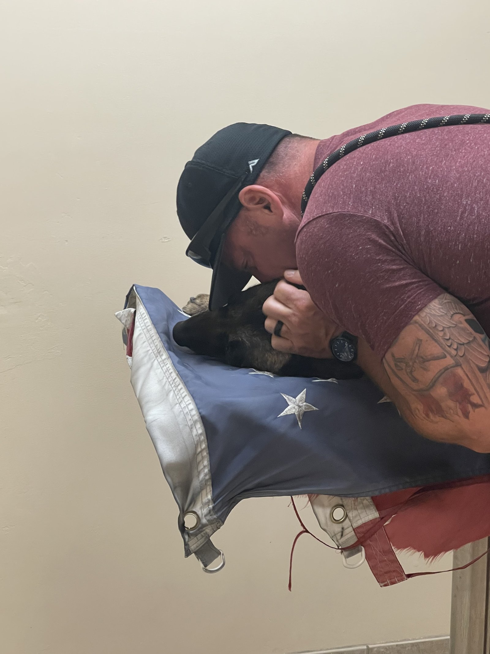 A handler bows his head against his K9 partner resting on an American flag, honoring the line-of-duty loss that inspired Bakersfield Pet Crematory.