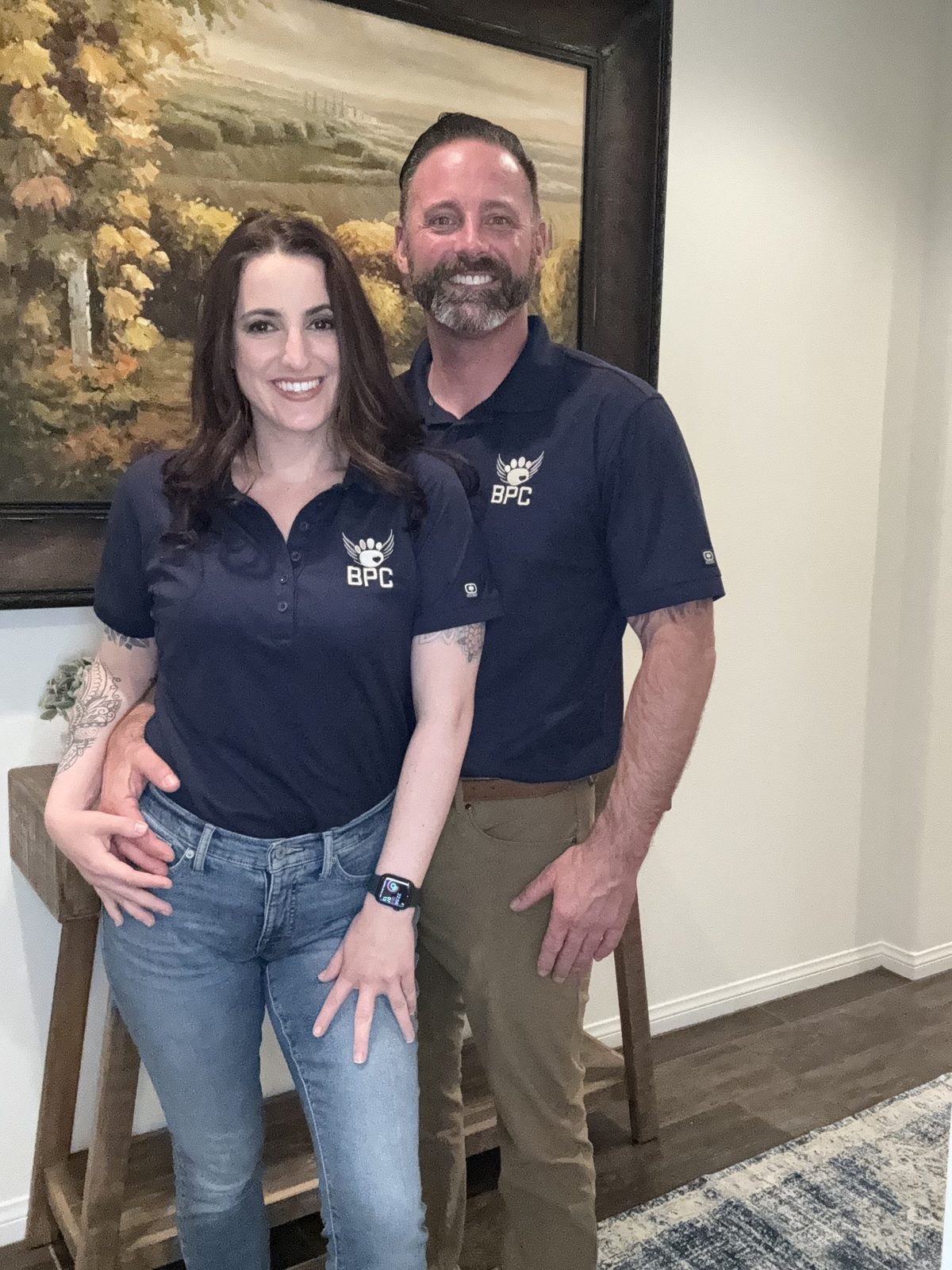 The owners of Bakersfield Pet Crematory, a couple in matching navy BPC polo shirts, smiling together inside their local facility